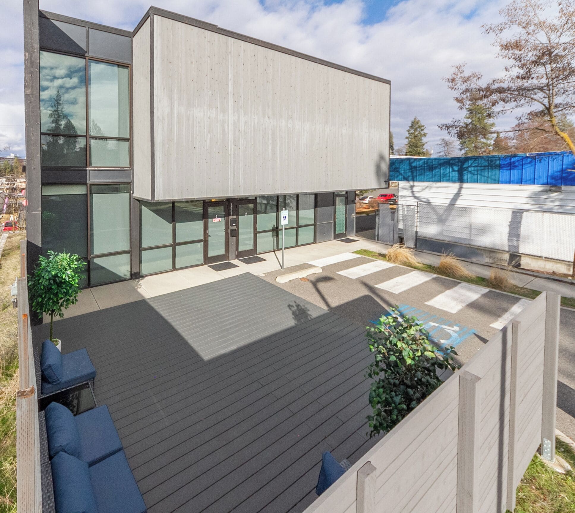 Un bâtiment moderne doté d’un toit plat, de grandes fenêtres et d’une terrasse en bois avec des sièges.