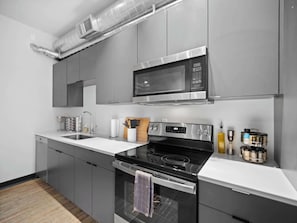 A modern kitchen with grey cabinets, a stainless steel microwave, a black stove, and a built-in oven.