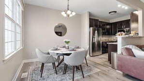A modern kitchen with dark cabinets, a stainless steel refrigerator, and a dining area with a round table and chairs. - Beautiful Townhouse located between Raleigh & Cary (Raleigh)