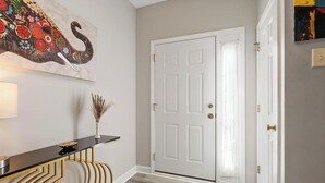 A hallway with a white door, a black console table, a vase with dried plants, and a colorful elephant painting on the wall. - Beautiful Townhouse located between Raleigh & Cary (Raleigh)