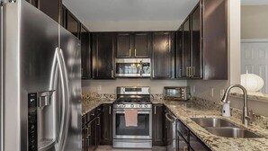 A modern kitchen with dark cabinets, stainless steel appliances, granite countertops, and a built-in oven. - Beautiful Townhouse located between Raleigh & Cary (Raleigh)