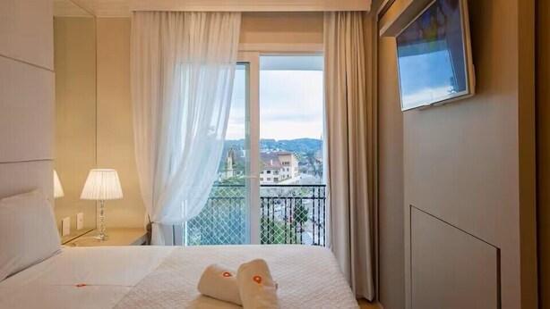 Une chambre d’hôtel avec un lit, une table de chevet, une lampe, une fenêtre avec des rideaux et une vue sur des immeubles.