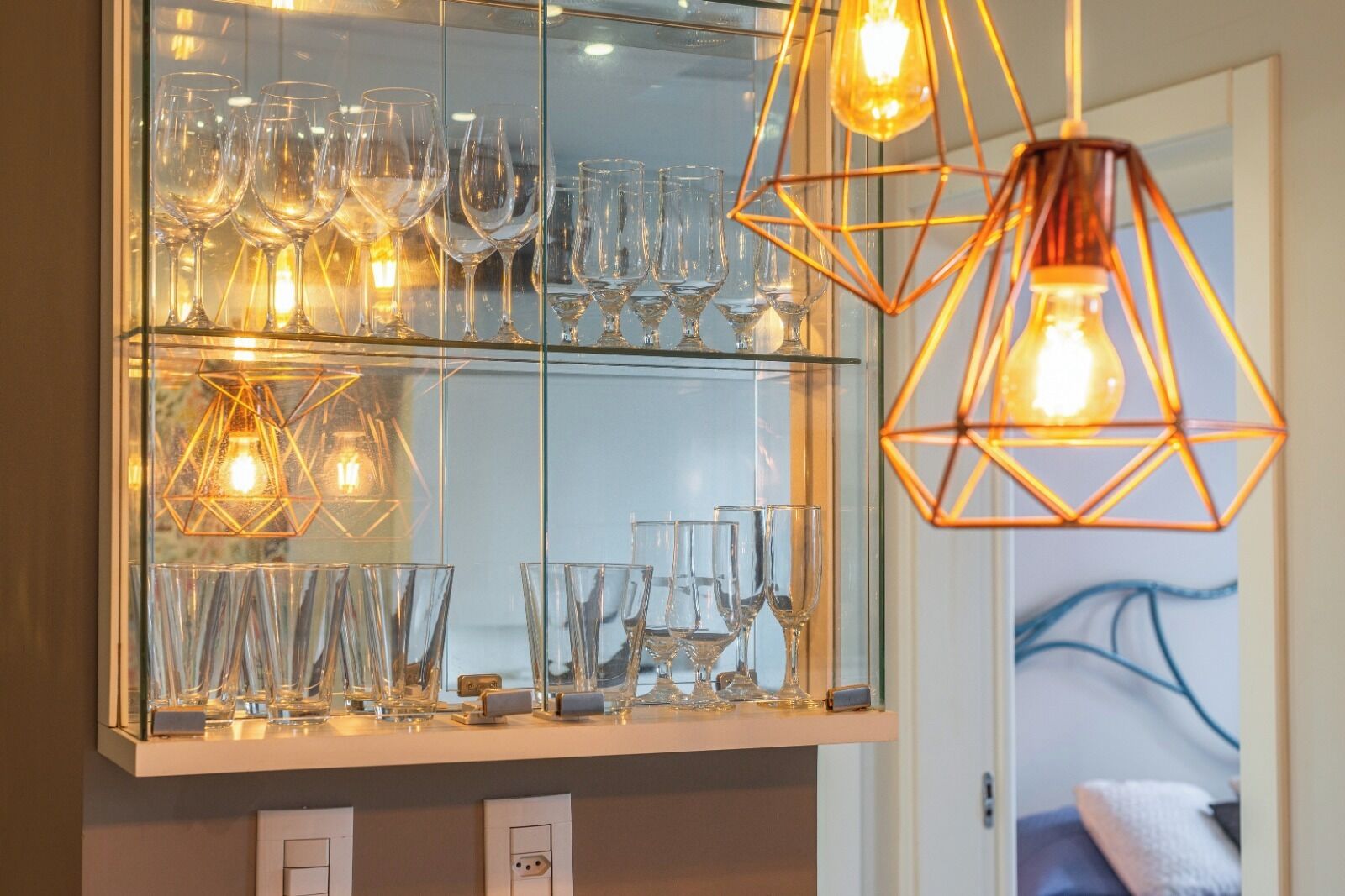 A glass-fronted display case with various glassware and geometric pendant lights.