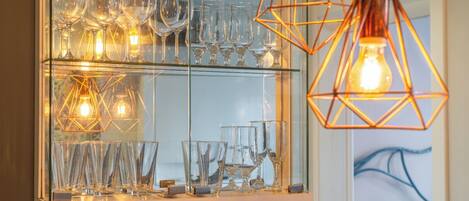 A glass-fronted display case with various glassware and geometric pendant lights.