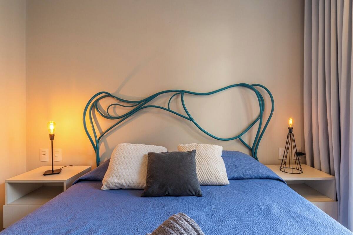 A bed with a blue bedspread, two white pillows, and a dark gray pillow. There are two bedside tables with lamps on either side of the bed.