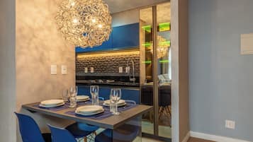A modern dining area with a table set for four, a chandelier, and a kitchen in the background.