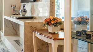 Un comptoir en marbre orné d’un vase de fleurs, un téléviseur fixé au-dessus, et une vitrine en verre contenant des tasses à café.