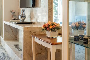 A marble counter with a vase of flowers, a television above, and a glass display case with coffee mugs.