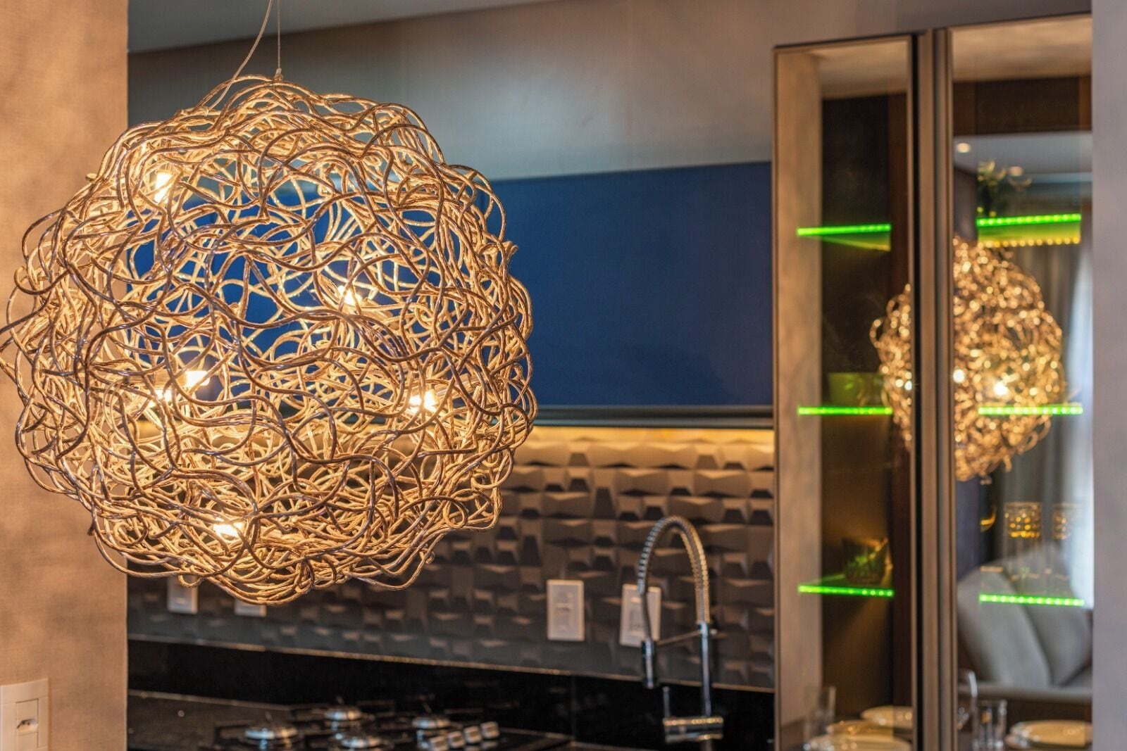 A spherical chandelier with multiple light bulbs, a modern kitchen with a black countertop, and a mirror reflecting the chandelier.