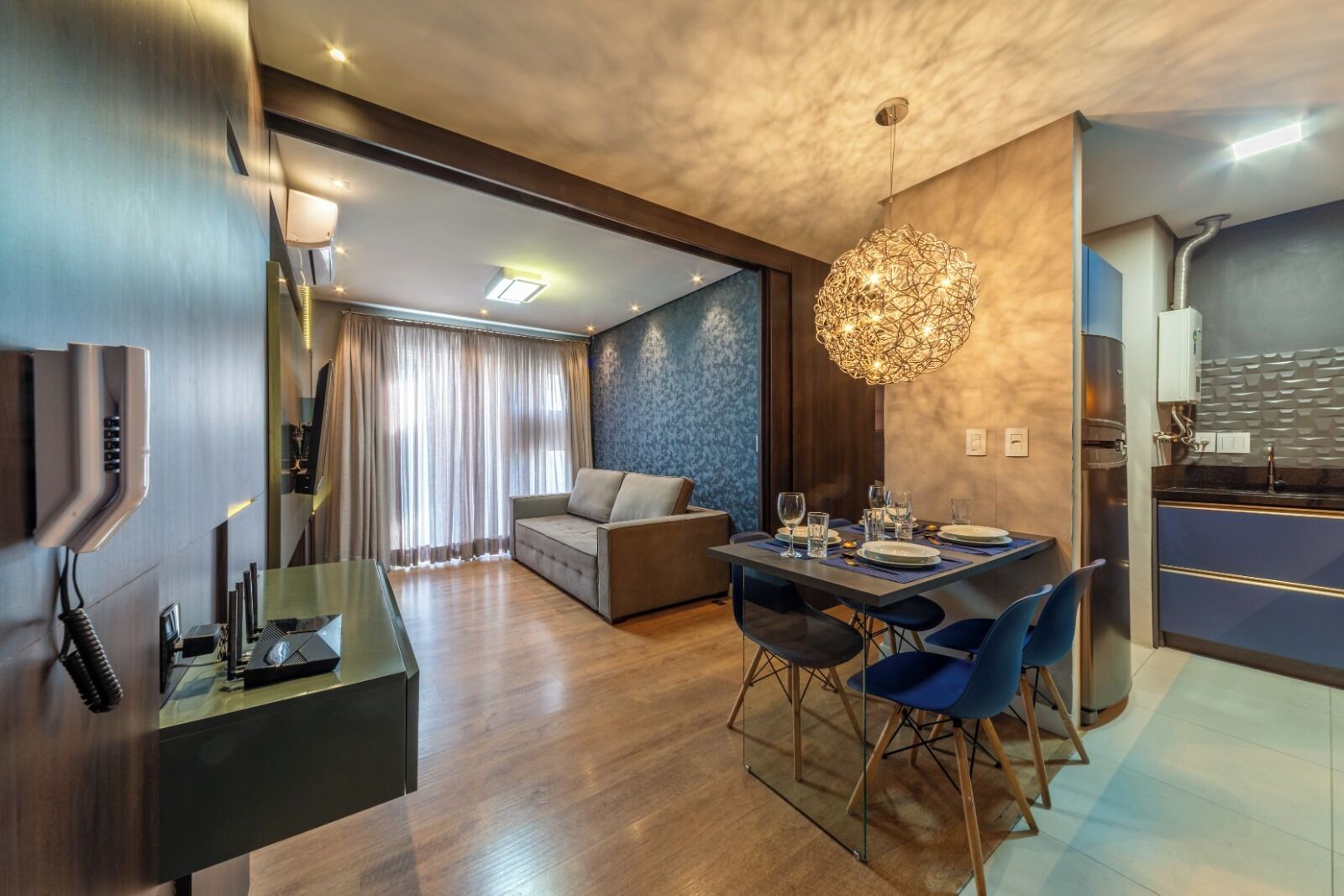 Quarto de hotel moderno com área de jantar, sofá, televisão e cozinha.