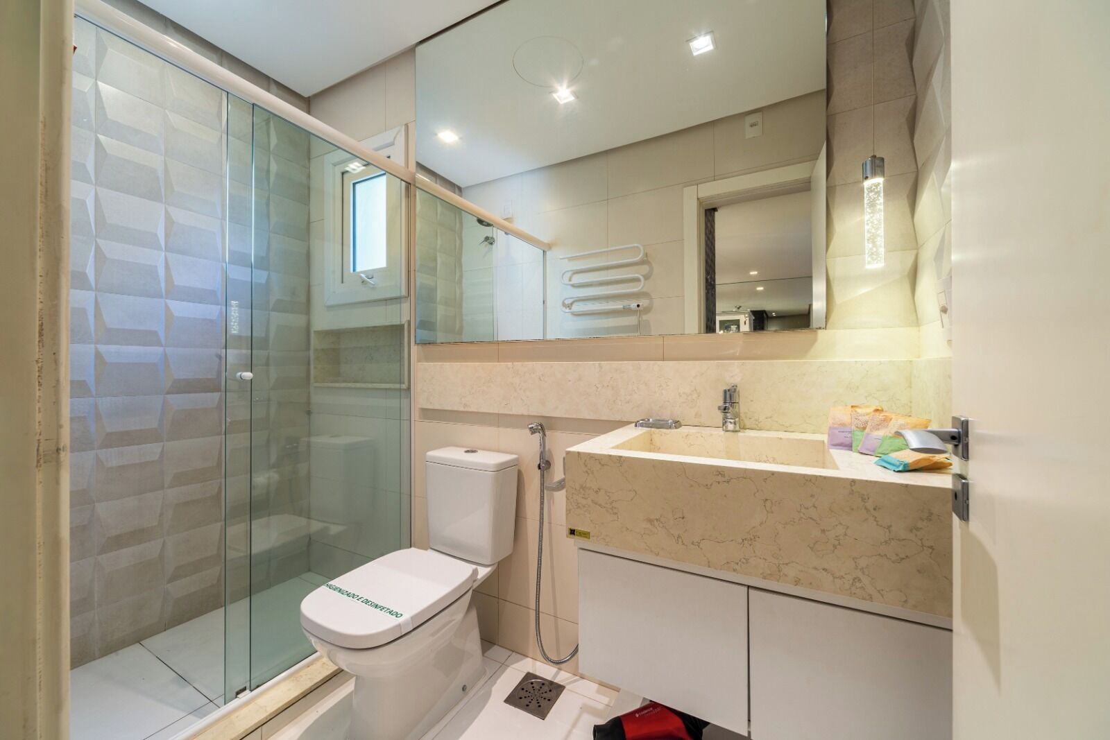 Un baño moderno con cabina de ducha de vidrio, inodoro, lavabo con encimera de mármol y espejo sobre el lavabo.