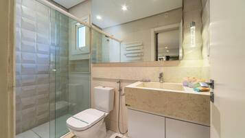Un baño moderno con cabina de ducha de vidrio, inodoro, lavabo con encimera de mármol y espejo sobre el lavabo.