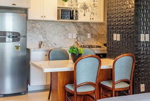 Una cocina con encimera de mármol, refrigerador de acero inoxidable, una araña y pared con textura.