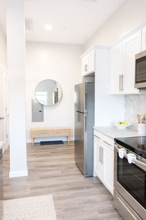 A modern kitchen with white cabinetry, a stainless steel refrigerator, and an oven. - King Spacious Yale Getaway near Wooster Sq Park (New Haven)