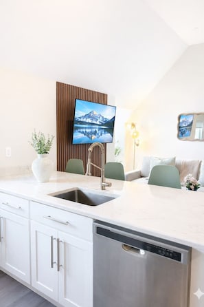 A modern kitchen with a built-in dishwasher, a sink, and a flat-screen TV mounted on a wooden panel. - King Spacious Yale Getaway near Wooster Sq Park (New Haven)