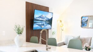Eine moderne Küche mit eingebautem Geschirrspüler, einer Spüle und einem Flachbildfernseher, der an einer Holzvertäfelung befestigt ist. Zwei Stühle und ein Sofa befinden sich im Raum, über dem Sofa hängt ein Spiegel.
