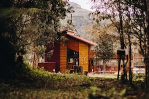 Eine Holzhütte mit Balkon, umgeben von Bäumen und einem Berg im Hintergrund.