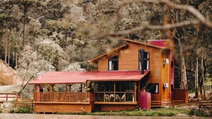 Een houten chalet met een rood dak, een balkon en uitzicht op een bebost helling.
