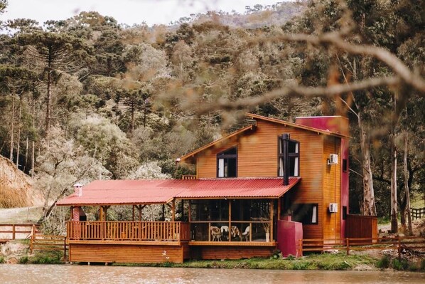 Una cabaña de madera con techo rojo, un balcón y vistas a un promontorio boscoso.
