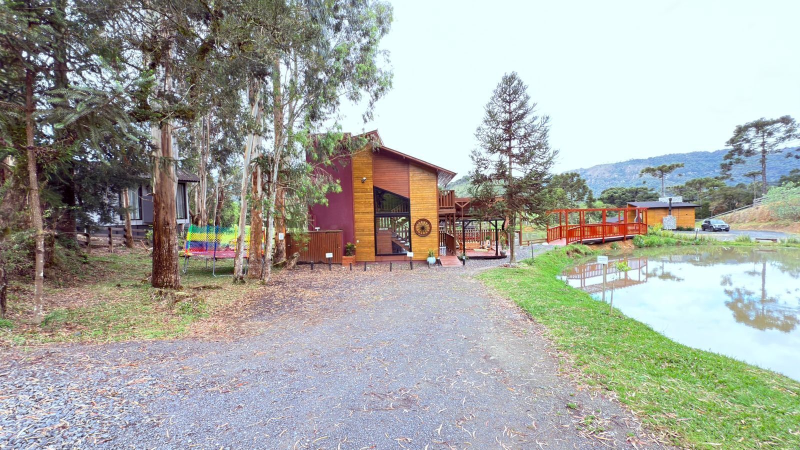 A building with a wooden exterior and a red door, surrounded by trees and a small pond.