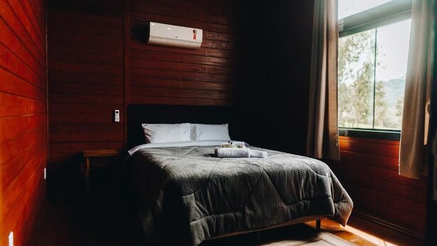 A bedroom with a bed, a window, and an air conditioning unit. - Chalé Aconchego  (Urubici)