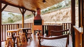 A wooden deck with a brick fireplace, wooden benches, and tables. - Chalé Aconchego  (Urubici)