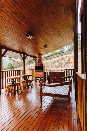 A wooden deck with a brick fireplace, wooden benches, and tables. - Chalé Aconchego  (Urubici)