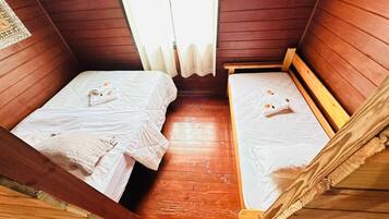 Una habitación pequeña y acogedora con dos camas de madera, cada una con una colcha blanca y un cojín pequeño. La habitación tiene paredes y suelo de madera.