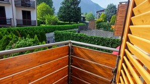 A balcony with wooden railings, a tiled floor, and a view of a mountain and buildings in the background.