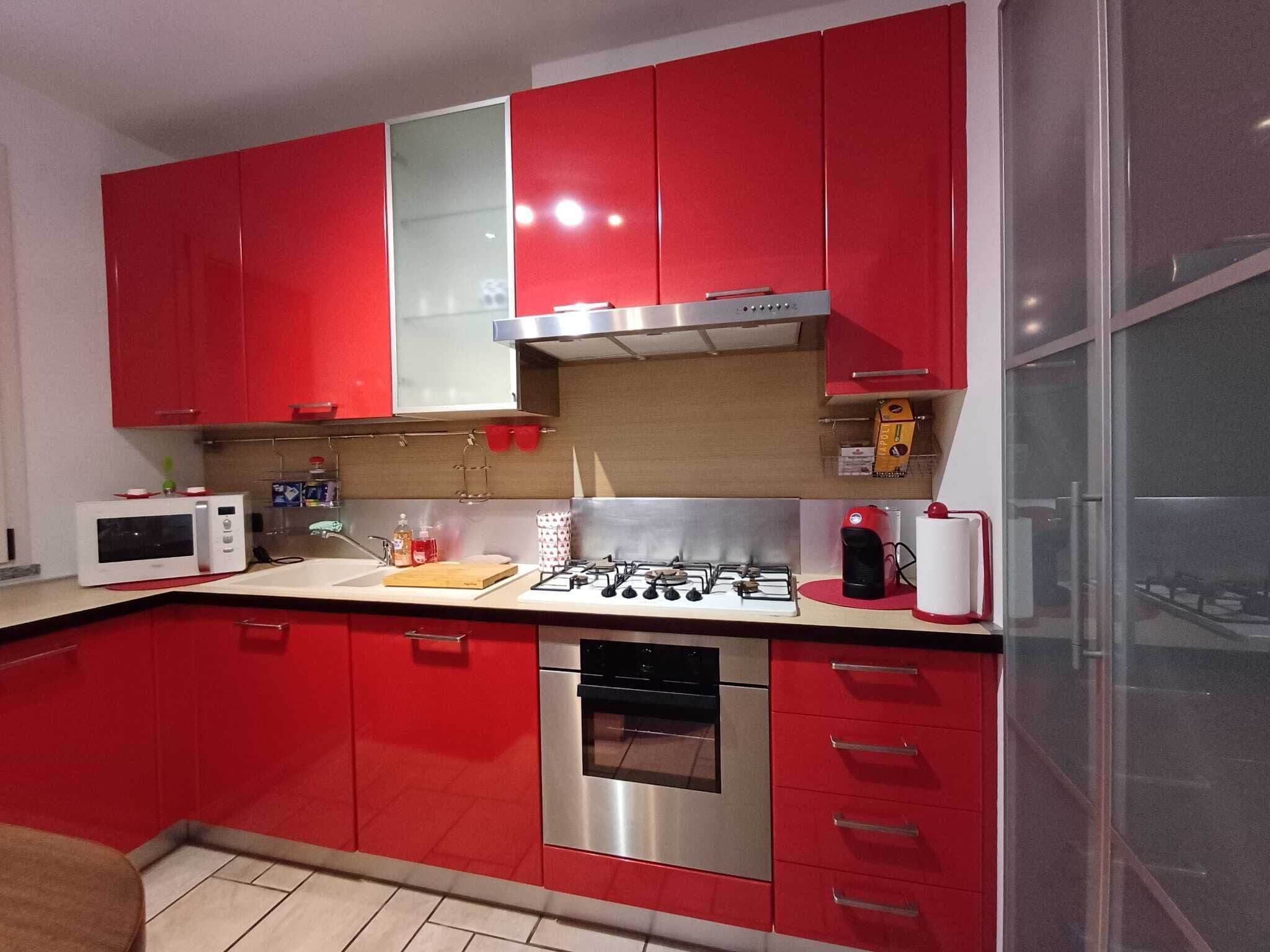 A modern kitchen with red cabinets, stainless steel appliances, and a tiled backsplash.