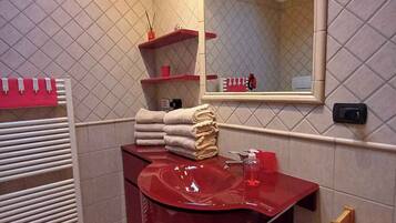 Un bagno con un lavandino rosso, uno specchio, un porta asciugamani e uno scaffale in legno.