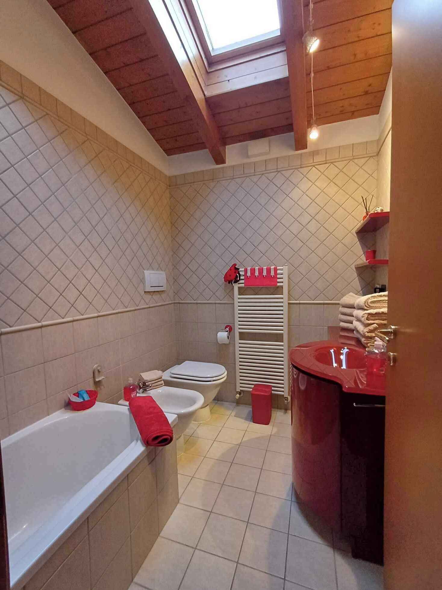 A bathroom with a bathtub, a toilet, a bidet, a red sink, and a towel rack.