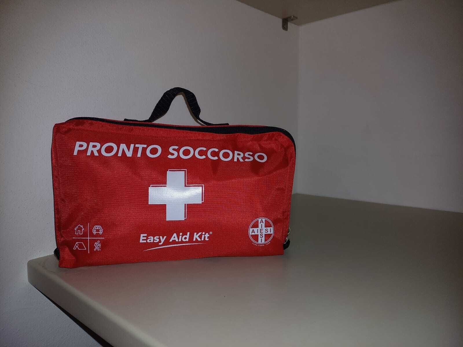Une trousse de premiers secours rouge, portant l’inscription « PRONTO SOCCORSO » en lettres blanches, ainsi qu’une croix blanche et le texte « Trousse de premiers secours facile d’utilisation ».