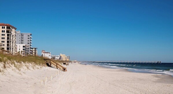 A beach with a wooden boardwalk leading to a pier.