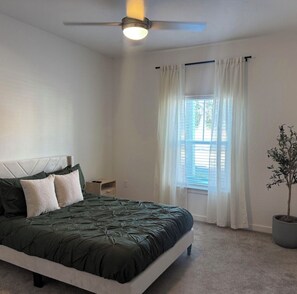 Une chambre à coucher avec un lit, un ventilateur de plafond, une fenêtre avec des rideaux et une plante en pot.