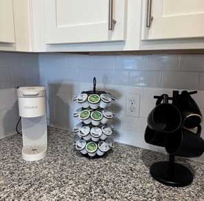 A kitchen with white cabinets, a Keurig coffee maker, a mug rack, and a coffee machine. - Azure Luxe Haven Near TPC, Mayo Clinic & Beaches! (Jacksonville)