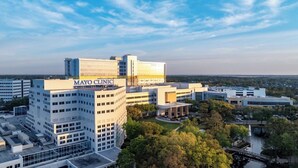 En byggnad som tillhör Mayo Clinic, med en modern arkitektonisk design, omgiven av träd och en klar himmel.