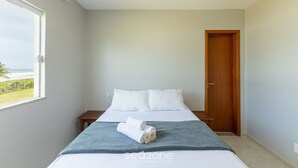 A bedroom with a bed, a wooden door, and a window with a view of the ocean.
