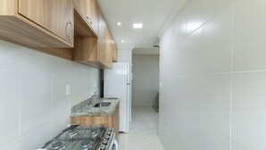 A narrow kitchen with wooden cabinets, a granite countertop, a white refrigerator, and a gas stove.