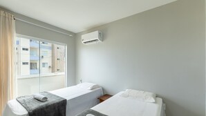 A hotel room with two single beds, a window with curtains, and an air conditioning unit on the wall.