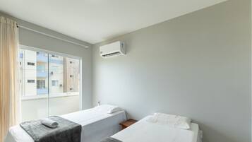A hotel room with two single beds, a window with curtains, and an air conditioning unit on the wall.