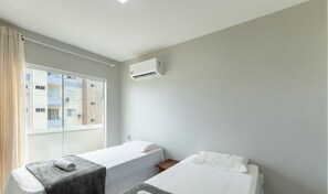 A hotel room with two single beds, a window with curtains, and an air conditioning unit on the wall. - Aptos in Beachfront Condominium in Ilheus, BA - Cals (Ilhéus)