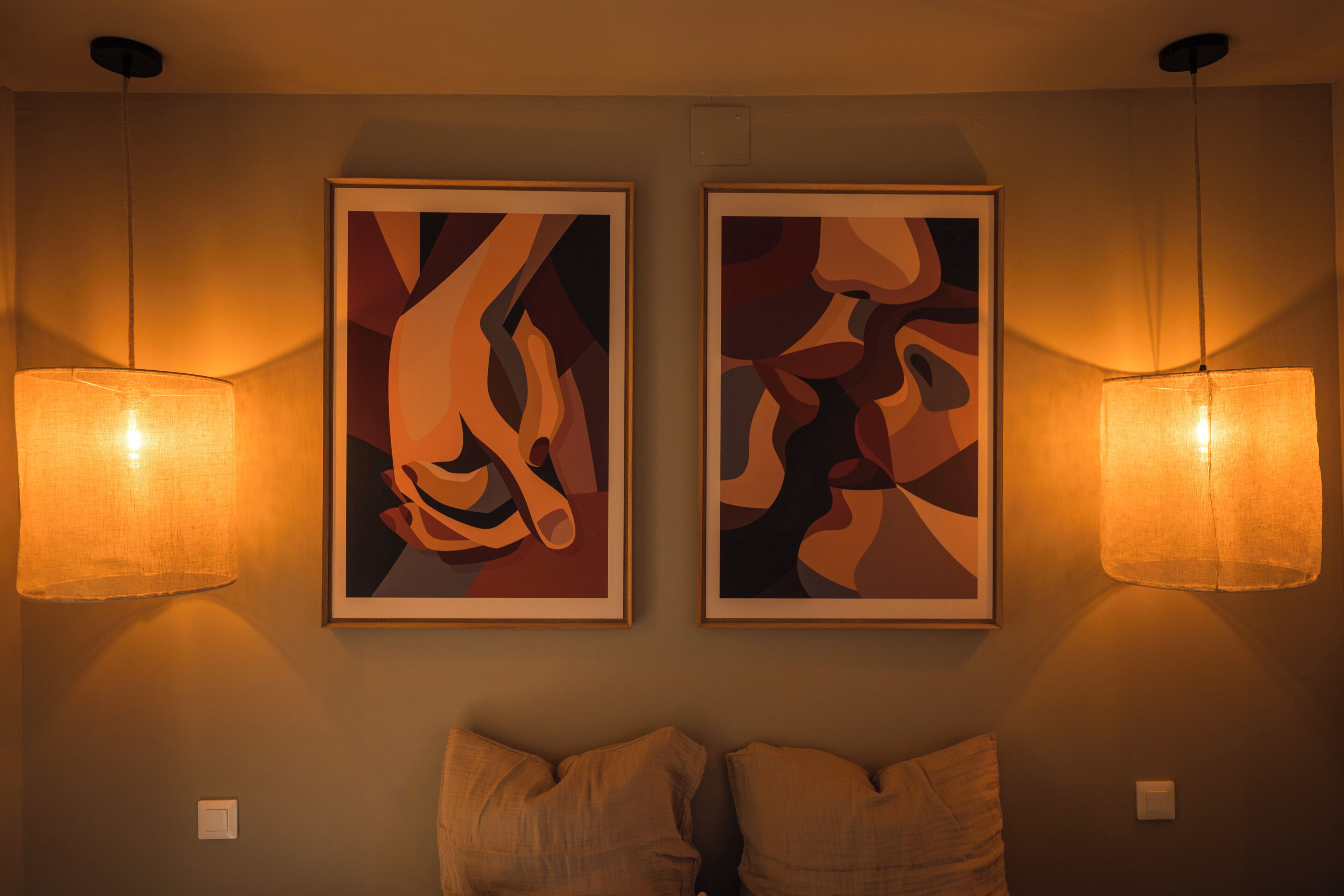 Deux tableaux abstraits sont accrochés au mur, au-dessus d’un lit, et deux lampes de chevet sont posées de part et d’autre.