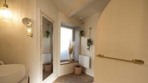 Une salle de bain avec un grand miroir, des toilettes, un lavabo et une fenêtre ornée de plantes.