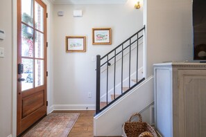 A hallway with a wooden door, a staircase with black railings, and two framed pictures on the wall. - The Alexa, 3BR Retreat by Velvet Ditch Villas (Oxford)