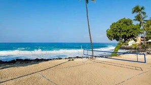 Una cancha de voleibol de playa con red, palmeras y olas del océano.
