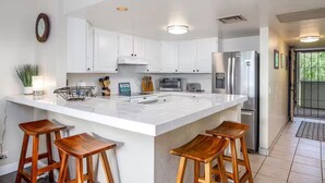 Una cocina moderna con armarios blancos, una isla grande con taburetes, electrodomésticos de acero inoxidable y un reloj en la pared.