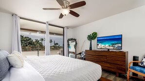 Un dormitorio con cama, cómoda de madera, televisor y balcón con vista al océano.