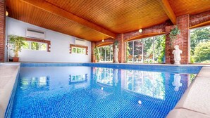 Ein Innenpool mit Holzbalkendecke und Backsteinwänden, umgeben von Fenstern und Topfpflanzen.