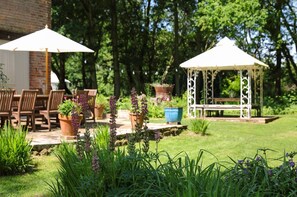 An outdoor patio with wooden chairs and tables, a gazebo, and potted plants. - The Brick House & Annexe (Beaulieu)